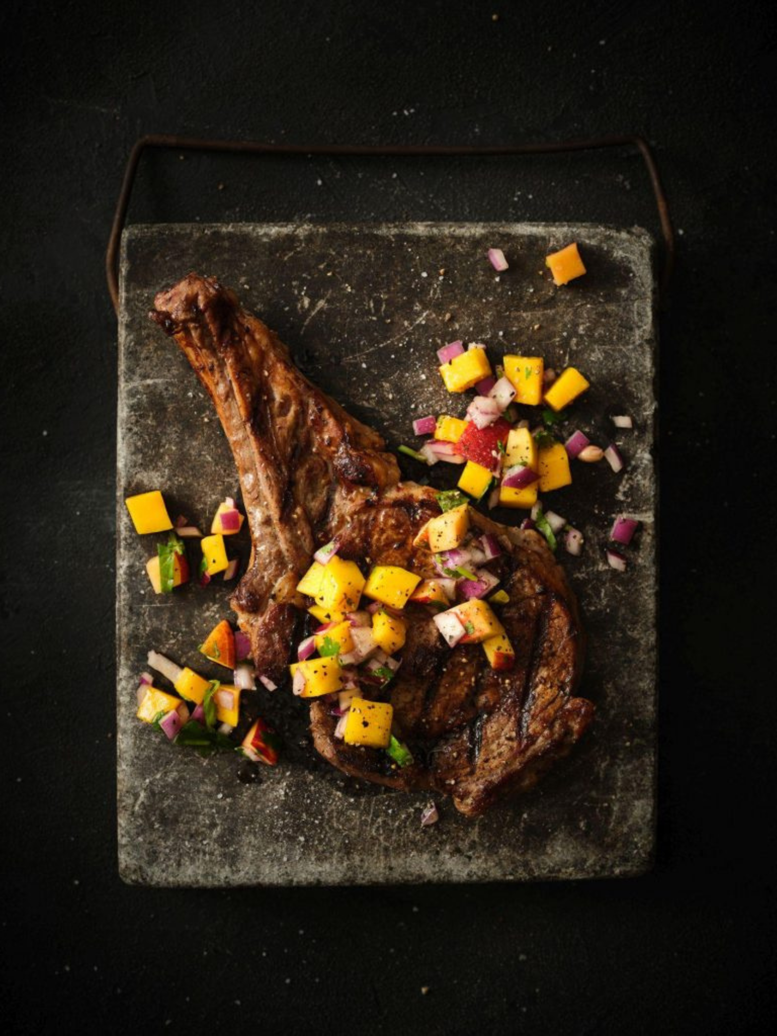 A thick cut veal loin chop resting on a pan of sauteed mushrooms.